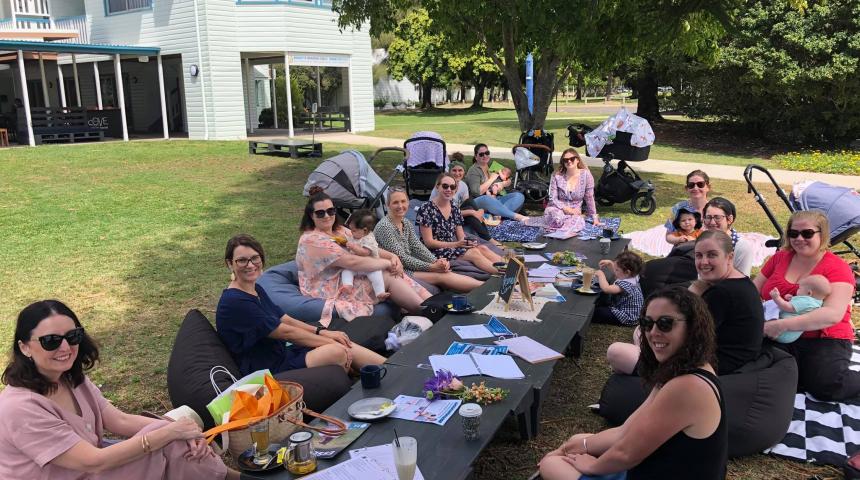 Group of mothers at outdoor cafe sitting in a circle with babies and prams. 