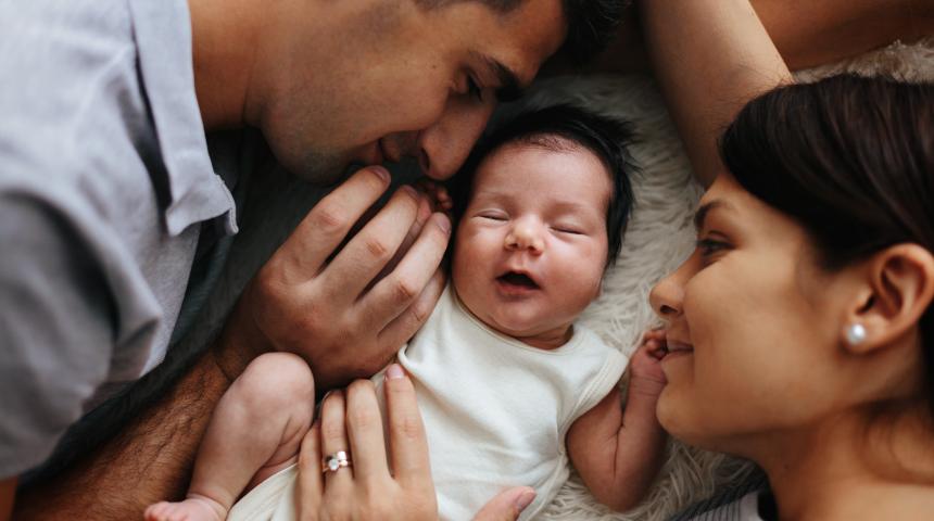 A mother and father smile at the newborn baby lying between them.