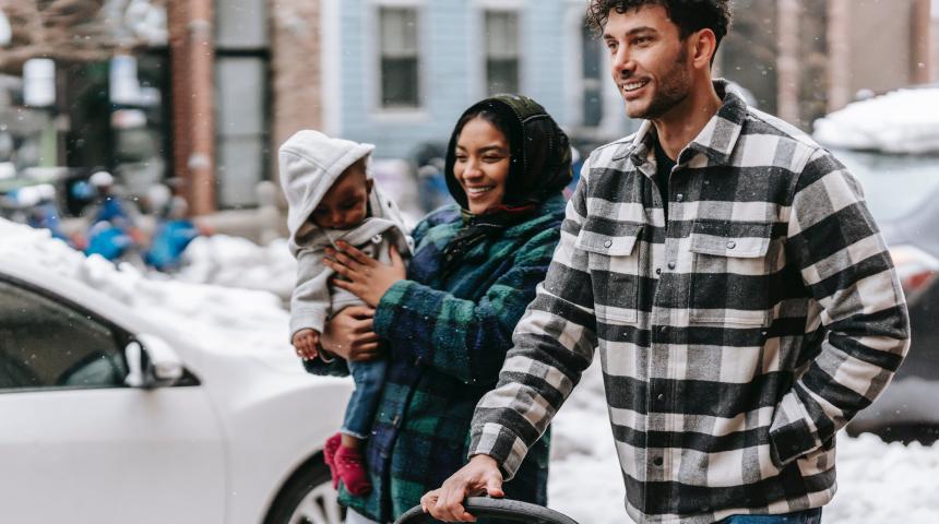 mother carrying infant and father pushing pram along footpath