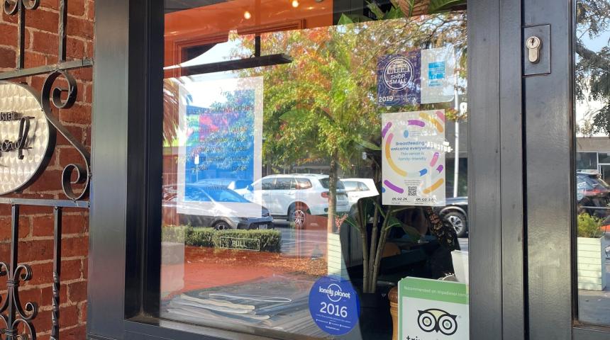 Looking into a cafe from the outside through the glass door with the Breastfeeding is Welcome Everywhere sticker displayed 