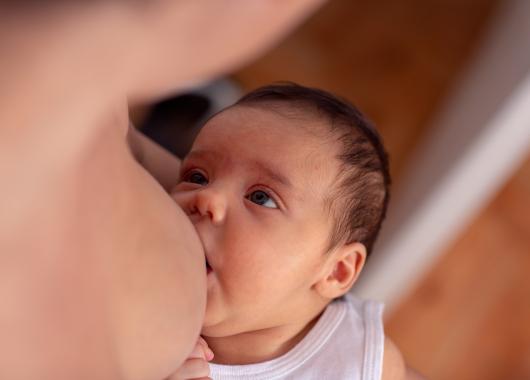 A newborn baby looks up at their mother while breastfeeding.