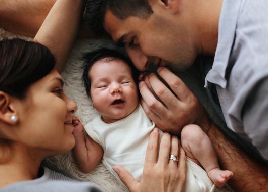 A mother and father smile at the newborn baby lying between them.