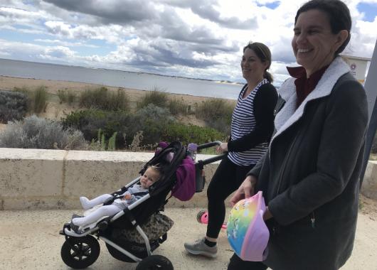 Two adults outside walking with one adult pushing a baby in a stroller
