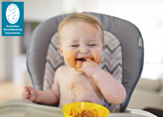 Baby sitting in a highchair, happily eating spaghetti