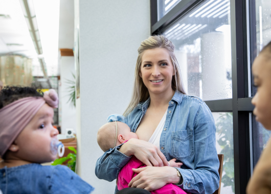 A woman breastfeeds her baby in the company of other mums and their children.