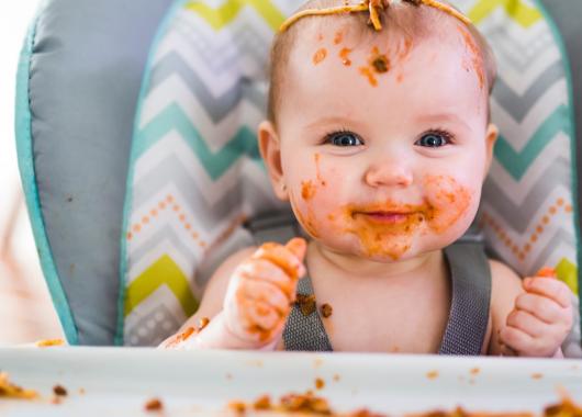baby sitting in high chair with food on its head and face
