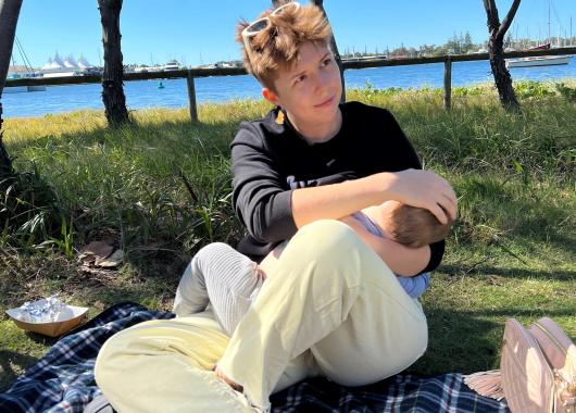 A woman breastfeeds her baby while sitting outside in the sunshine.