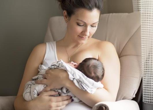 A mother breastfeeding her young baby looks down towards the baby's face