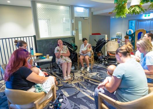 A group of mothers sitting in a circle chatting and some are breastfeeding babies.