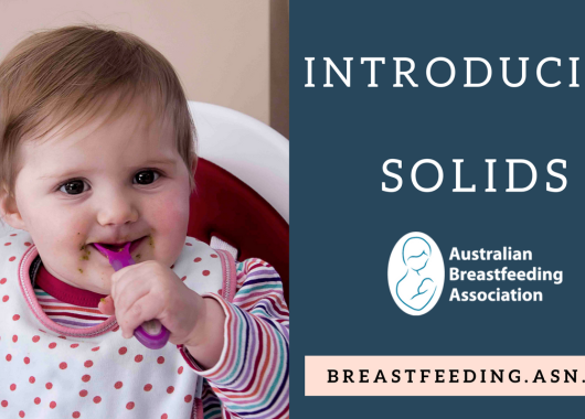 baby wearing stripe shirt and polka dot bib. Baby is in high chair and using a purple spoon