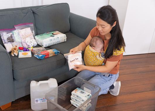 Woman with baby packing emergency supplies into a container.