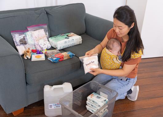 Woman with baby packing emergency supplies into a container.