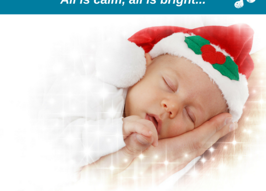 Baby asleep on a hand. Baby is wearing a Santa hat with holly and ivy on it.