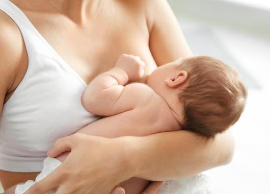 young baby being held to mother's breast, seen from the back, mother's face is not visible
