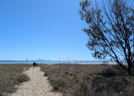 2 small children in the distance walk along a sandy beach access path on a beautiful clear day