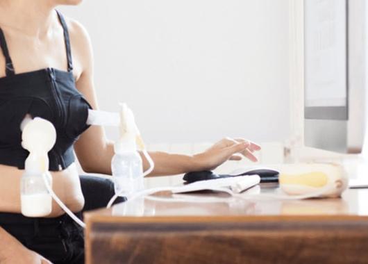 A woman working at a computer while wearing a double electric breast pump in a pumping bra