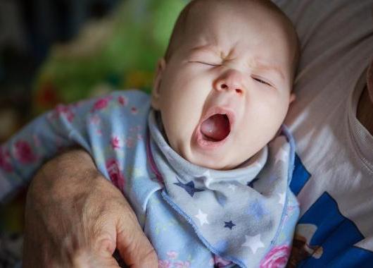 Baby in parents arm yawning widely