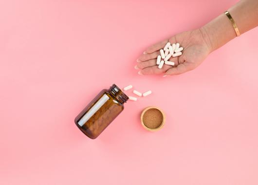 Image shows and open bottle of tablets lying on its side with some tablets spilled and some tablets being held in a women's hand