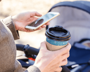 Mum holding takeaway cup of coffee with baby in pram alongside