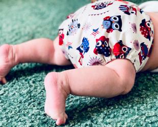An image of a baby crawling on carpet. The baby is wearing a modern cloth nappy with cute owls on it.