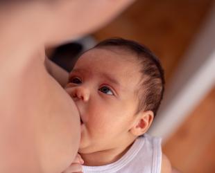 A newborn baby looks up at their mother while breastfeeding.