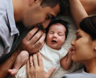 A mother and father smile at the newborn baby lying between them.