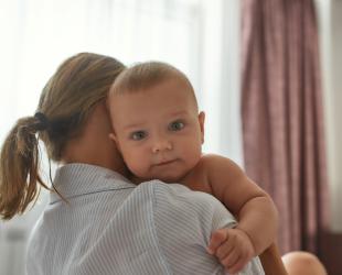 A baby looking over their mother's shoulder while being held.