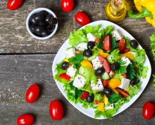 A platter of salad with scattered tomatoes, olives and vegetables on a table