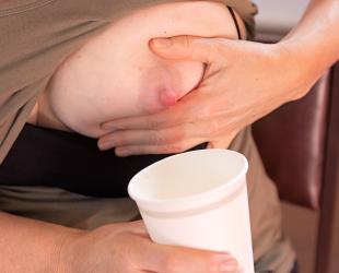 A woman hand expresses breastmilk into a paper cup during an emergency