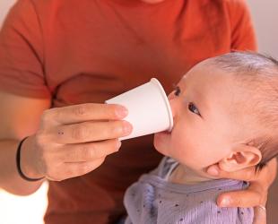 A baby drinks expressed breastmilk from a disposable paper cup in an emergency
