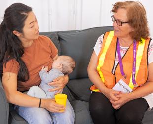 An emergencies volunteer sits with a breastfeeding mother and provides support