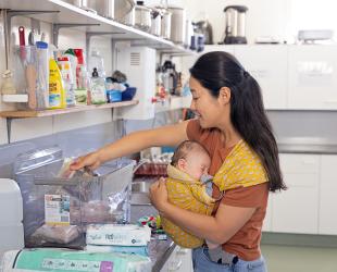 A woman with a young baby in a carrier sorts through emergency supplies