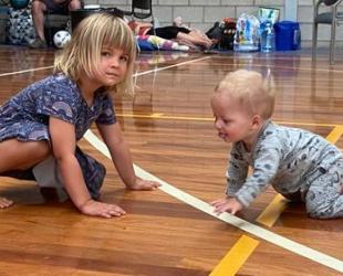 Young child and baby crawling on the floor of an evacuation centre.