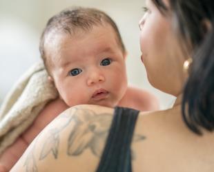 A baby looks over their mother's shoulder