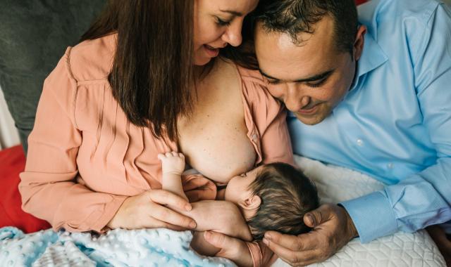 Happy multicultural family mum breastfeeding with dad alongside