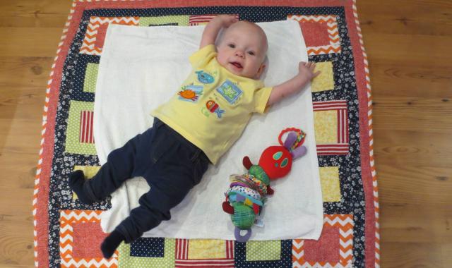 An image of a 4 month old baby laying on a rug with his hands in the air