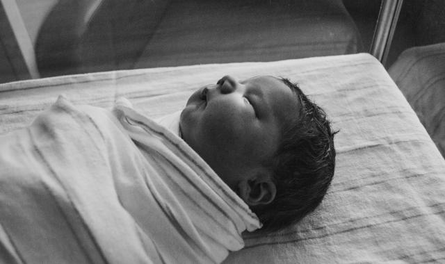 An image of a swaddled baby sleeping in a hospital cot.
