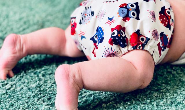 An image of a baby crawling on carpet. The baby is wearing a modern cloth nappy with cute owls on it.