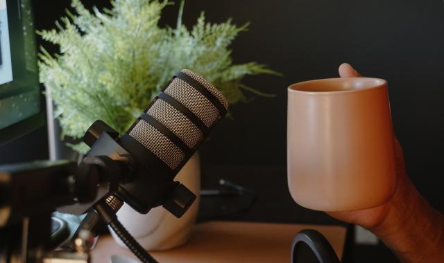 An image of a podcast microphone and someone holding a coffee cup.