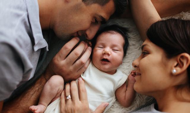 A mother and father smile at the newborn baby lying between them.