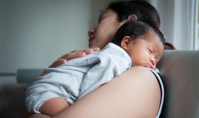 A mum holding her sleeping newborn baby.