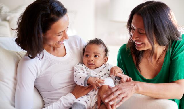 A mother, grandmother and baby sit together on the couch.