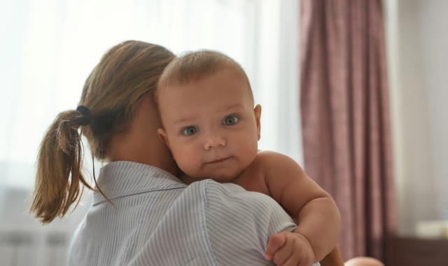A baby looking over their mother's shoulder while being held.