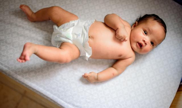 A picture of baby in a nappy laying on a mat. The baby is looking at the camera with a cute expression.