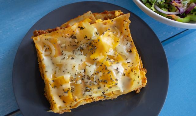A plate with a slice of lasagne, topped with melted cheese. A bowl of garden salad sits beside it.