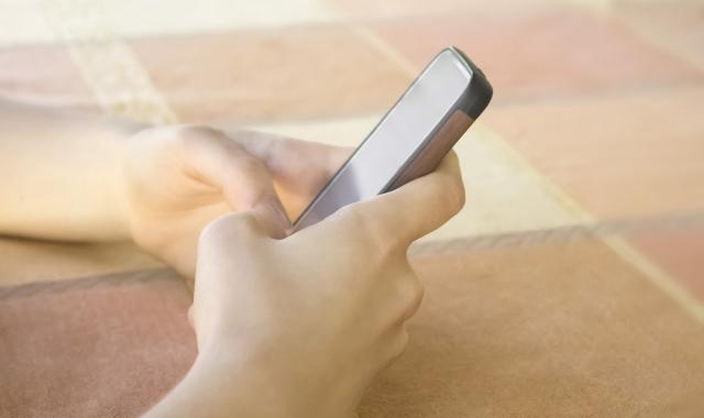 A woman's hands resting on a table cloth, holding a phone.