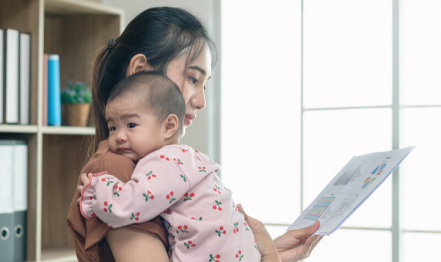 A woman is at work and holding her baby.