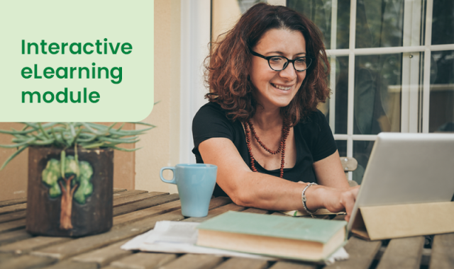 Woman sat at a laptop with a mug in front of her, smiling as she appears to work