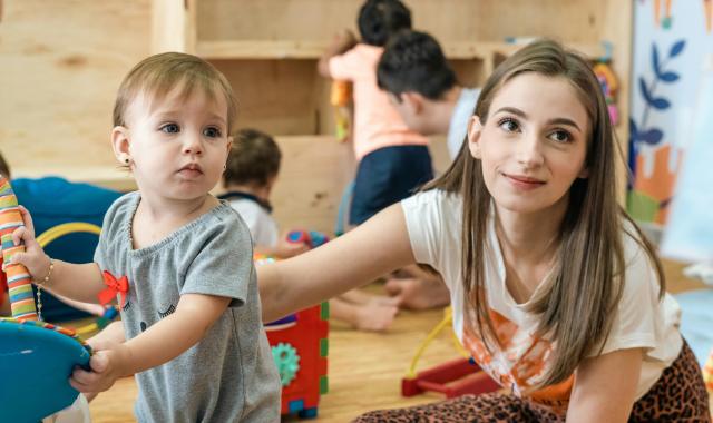 Educator sitting on the floor with a 1-year old at a child care centre