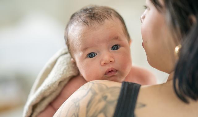 A baby looks over their mother's shoulder